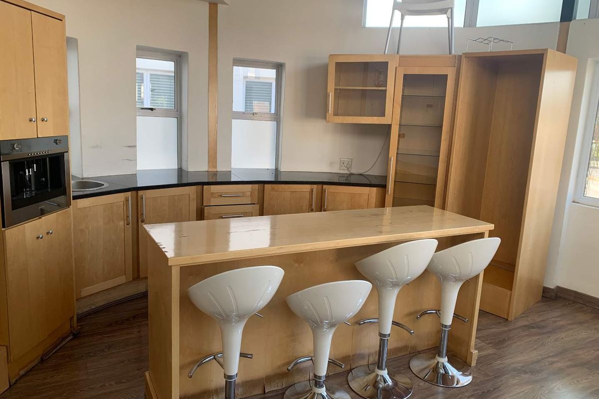 A functional kitchen area featuring light wood cabinetry, dark stone countertops, a built-in oven, and a central breakfast bar island.