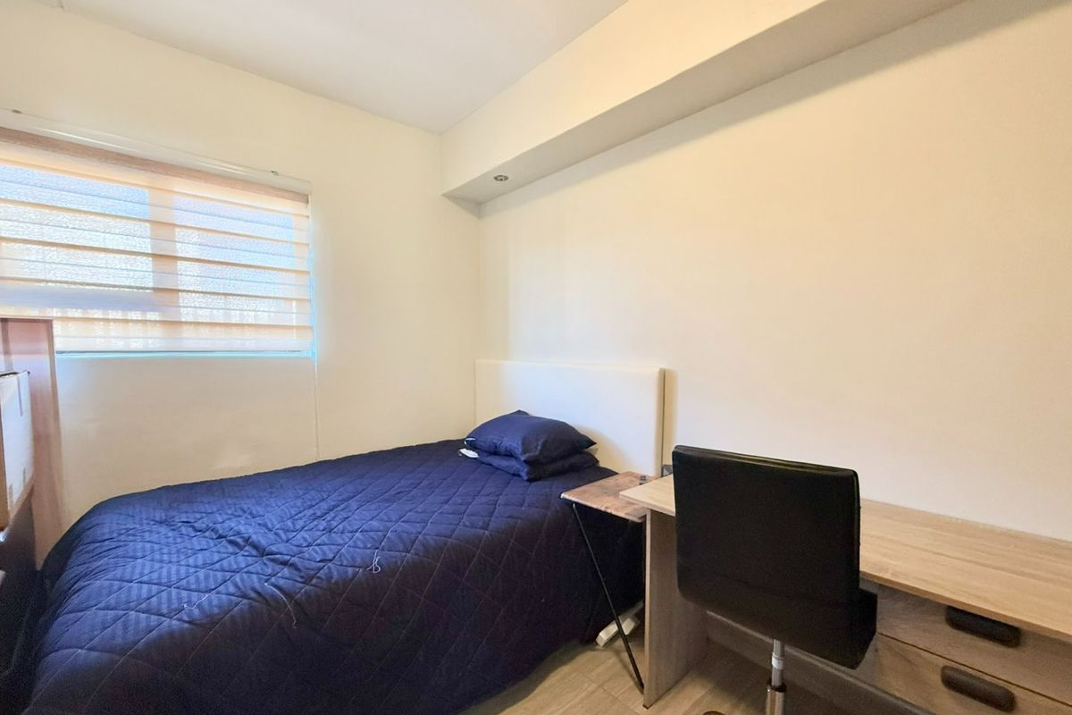 A functional bedroom featuring recessed ceiling lighting, neutral walls, and a built-in desk area with roller blinds for privacy.