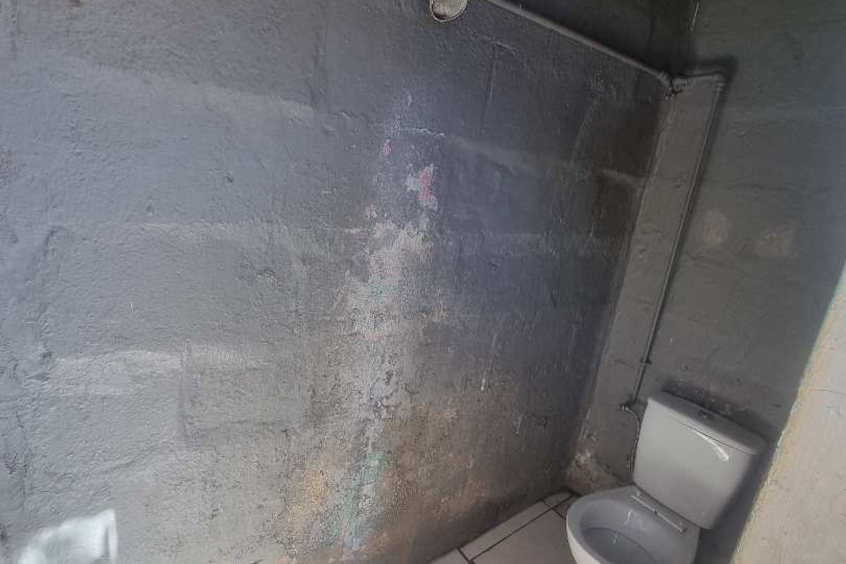A basic bathroom featuring a toilet and shower head with exposed concrete block walls and tiled flooring.