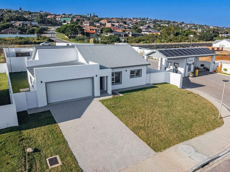 Aerial view of a modern single-story residential property featuring a paved driveway, garage, and surrounding landscaped garden within a secure estate.