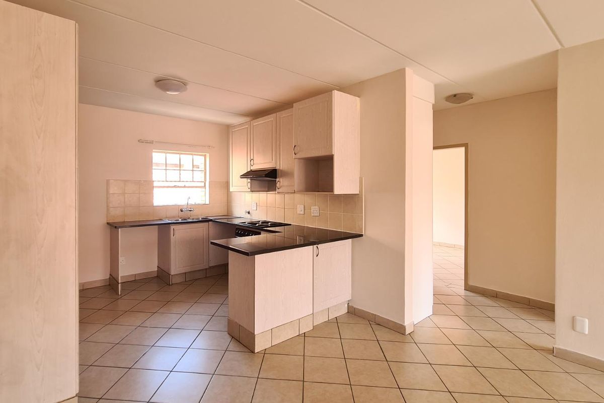 A clean, empty kitchen featuring light-toned built-in cabinetry, dark laminate countertops, tiled backsplash, and ceramic floor tiles.
