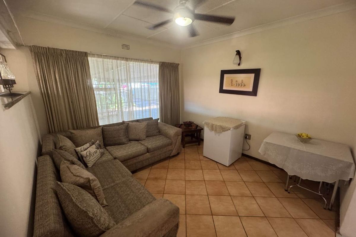 A living room featuring tiled flooring, a ceiling fan, and large windows with curtains, providing a functional and comfortable living space.