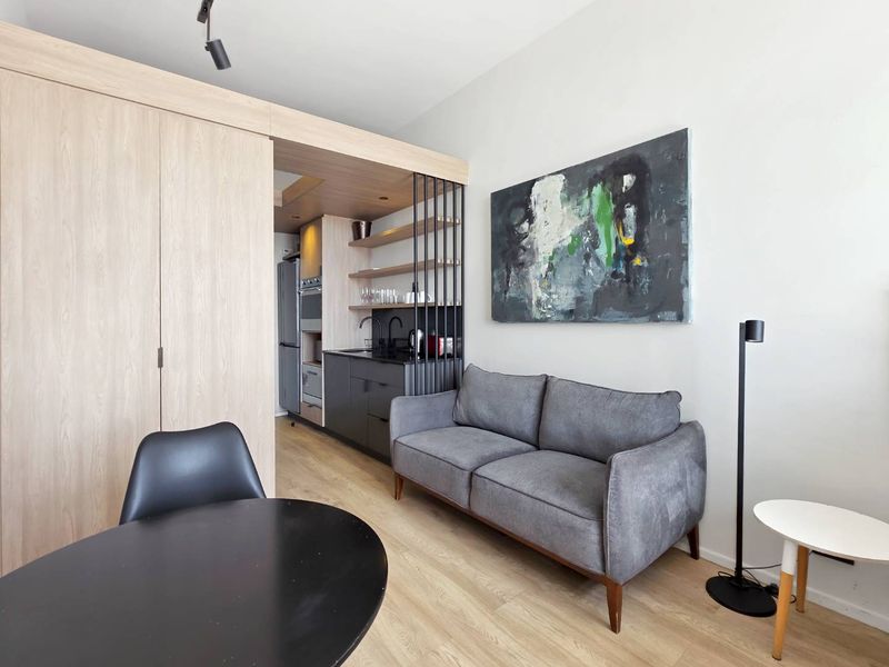 Modern open-plan living area featuring light wood-tone cabinetry, integrated shelving, and high-quality laminate flooring in a contemporary apartment setting.