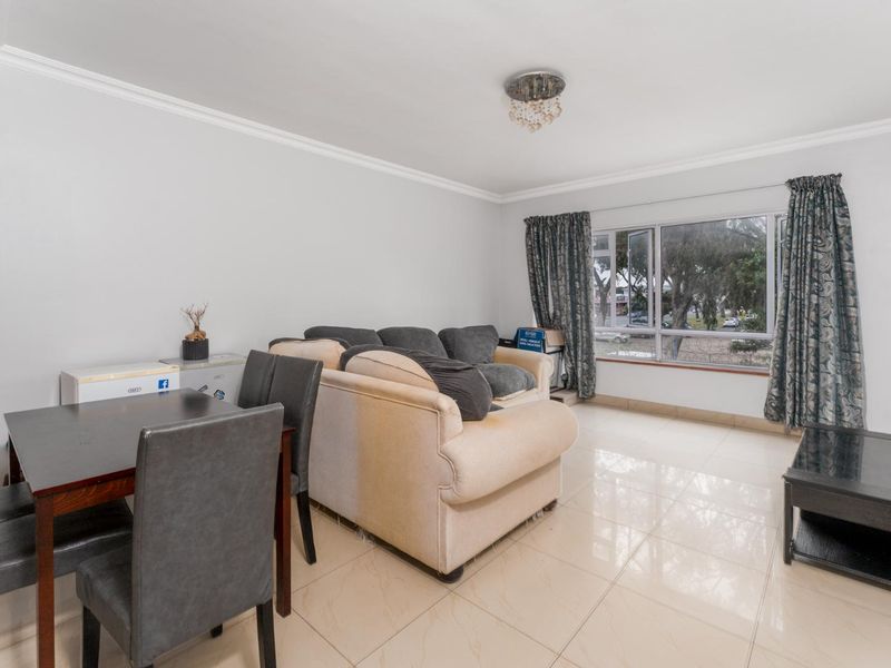 A bright living area featuring neutral tiled flooring, crown molding, and a large window providing natural light.