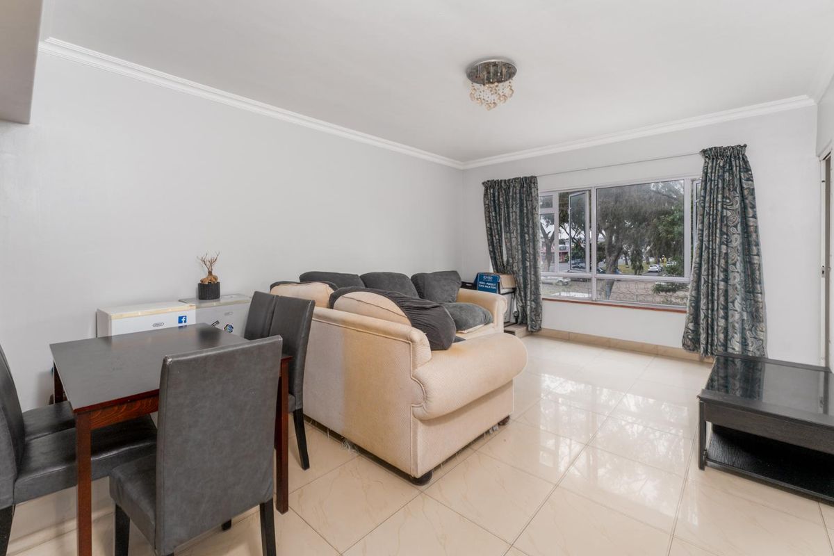 A bright living area featuring neutral tiled flooring, crown molding, and a large window providing natural light.