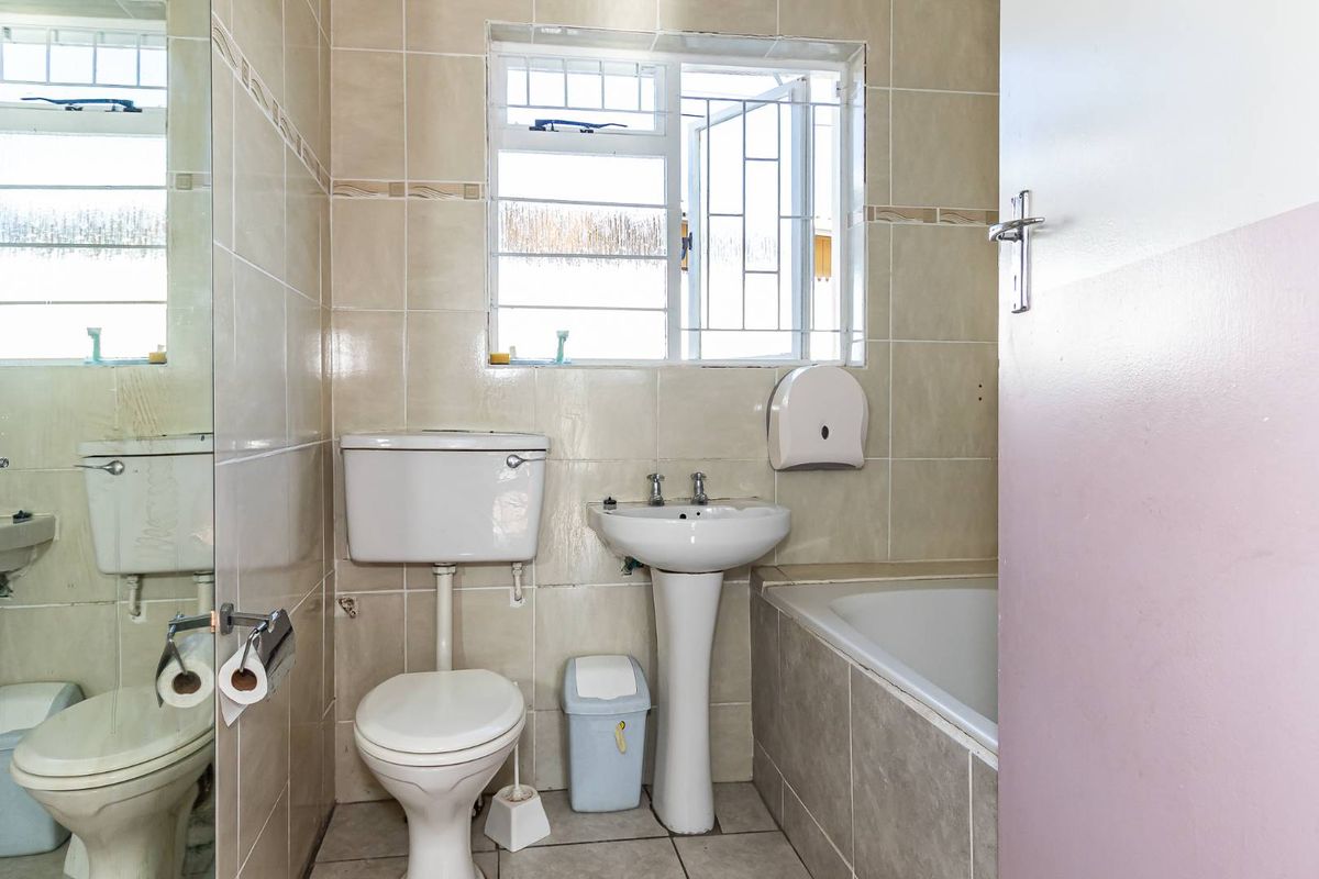 A functional bathroom featuring a pedestal basin, toilet, and a tiled bathtub with a window providing natural light.