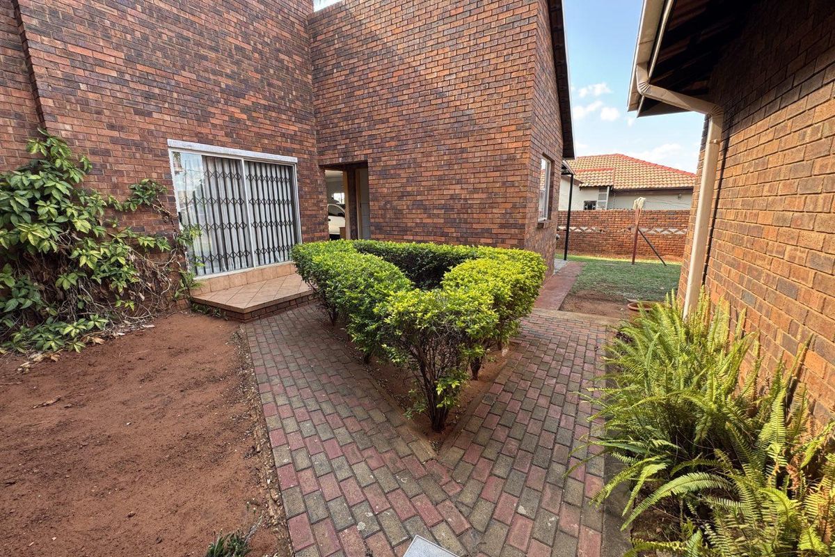 A rear exterior view of the property featuring face-brick walls, a paved walkway, and a small garden area with established shrubs.