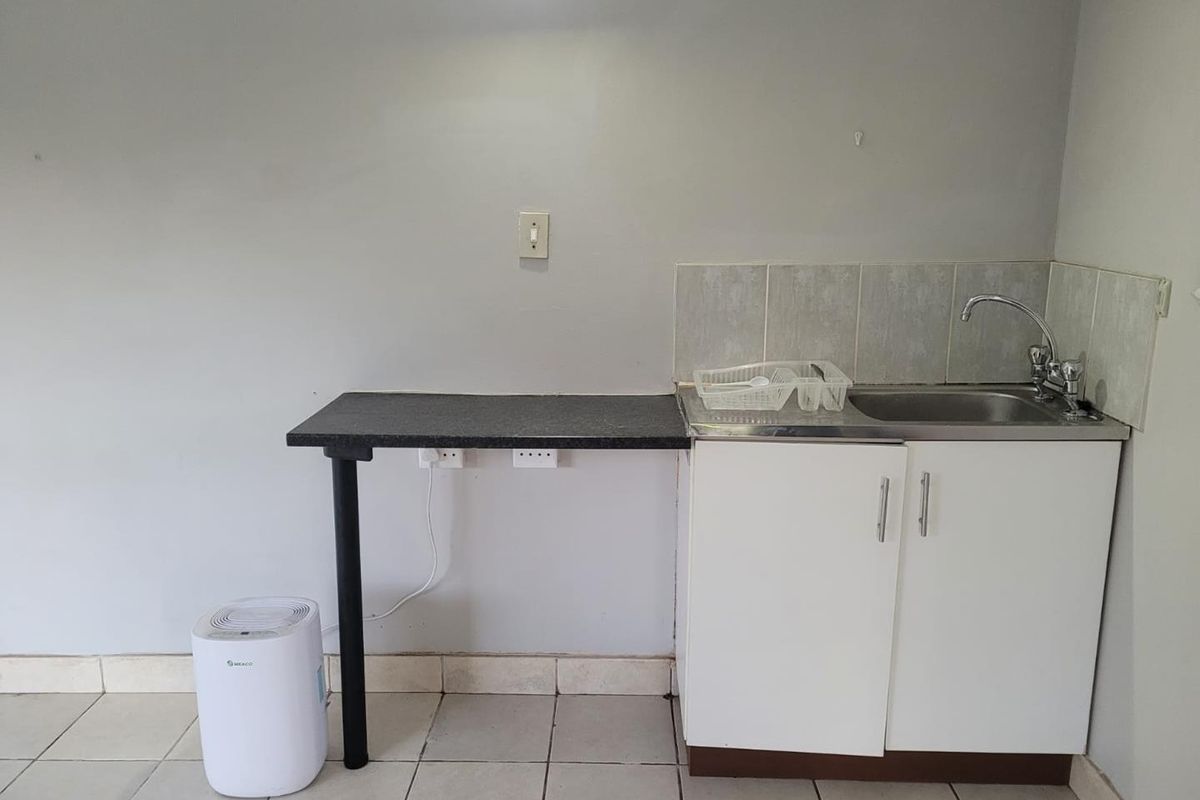 A compact kitchenette area featuring a stainless steel sink, tiled splashback, and basic base cabinetry with a small attached counter space.