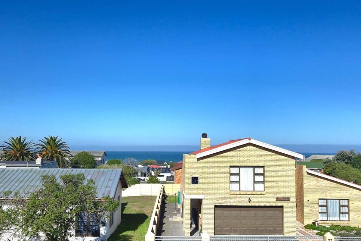 Elevated aerial view of a residential property featuring a brick facade, garage, and distant ocean views.