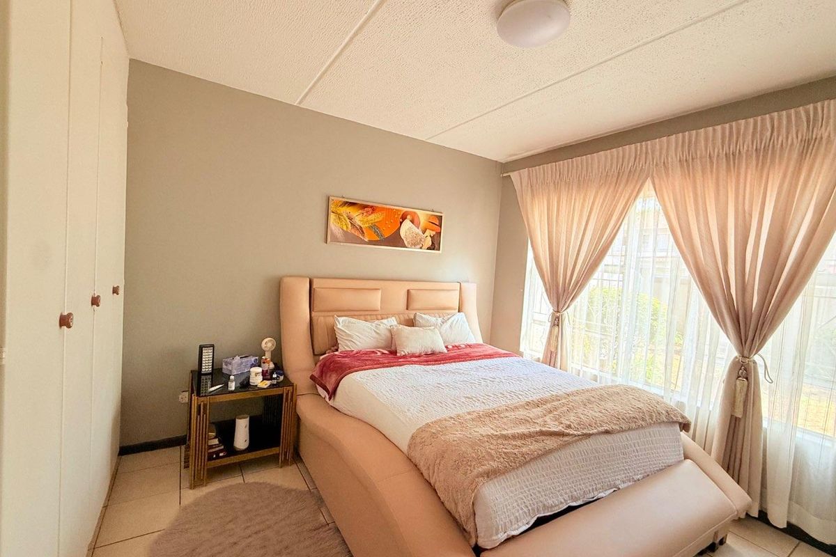 A well-lit bedroom featuring built-in floor-to-ceiling wardrobes, tiled flooring, and large windows with curtain tracks.