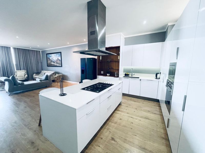 Modern open-plan living area featuring a sleek kitchen with a central island, gas hob, integrated appliances, and high-quality finishes throughout.