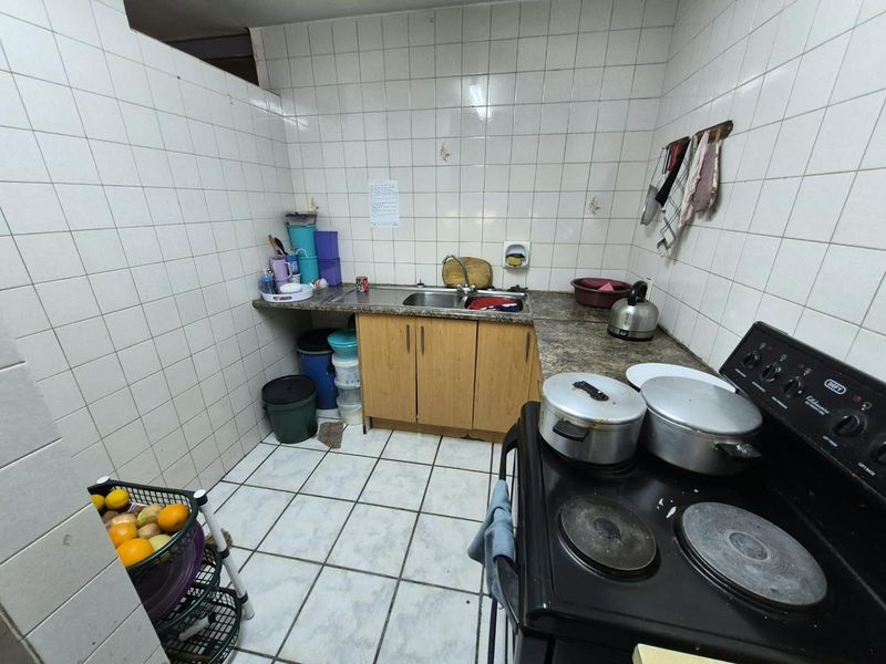 A compact kitchen featuring tiled walls and flooring, laminate countertops, a stainless steel sink, and a freestanding electric stove.
