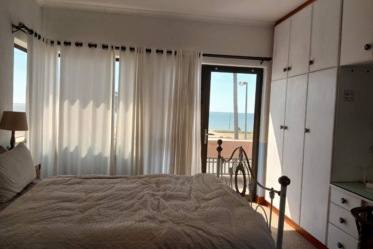 Bedroom featuring built-in floor-to-ceiling wardrobes, neutral flooring, and direct access to a balcony with scenic coastal views.