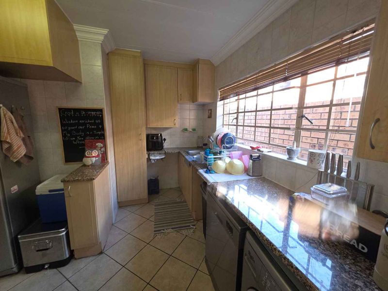 A functional kitchen featuring laminate cabinetry, granite countertops, tiled flooring, and a large window with venetian blinds.