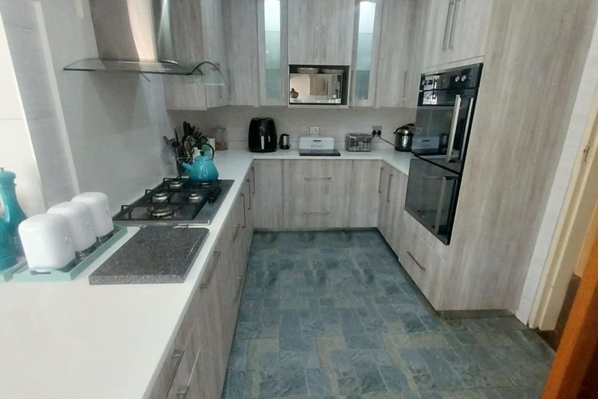 Modern U-shaped kitchen featuring light wood-grain cabinetry, stone countertops, built-in double oven, gas hob, and stainless steel extractor fan.