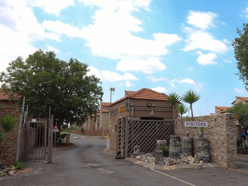 The entrance to the apartment complex features a secure gated access point with a guard house, electric fencing, and stone-clad boundary walls.