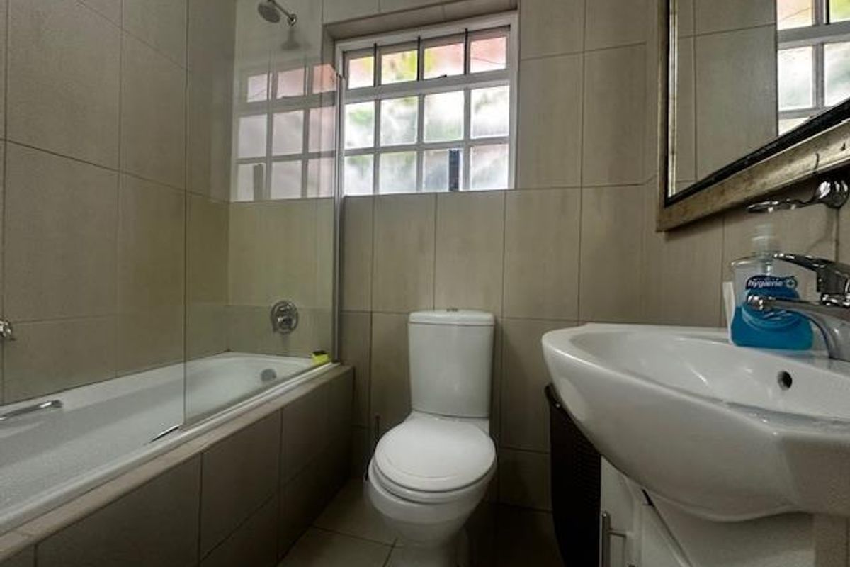A functional bathroom featuring a tiled bathtub with a glass shower screen, a white ceramic toilet, and a vanity basin with a chrome mixer tap.