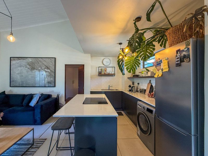 Modern open-plan kitchen featuring a central island with built-in hob, stone countertops, subway tile backsplash, and integrated laundry appliances under a vaulted ceiling.