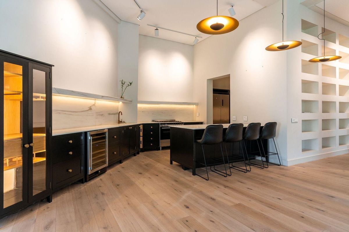 Modern open-plan kitchen featuring dark cabinetry, marble-style backsplash, integrated wine cooler, gas stove, and a central island with breakfast bar seating.