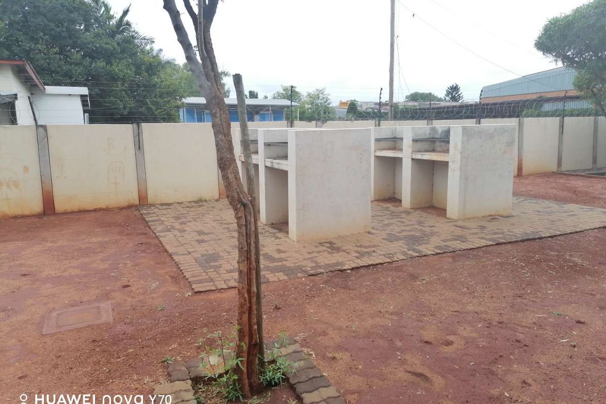 Outdoor communal area featuring built-in concrete braai stands on a paved base, situated within a fenced property perimeter.