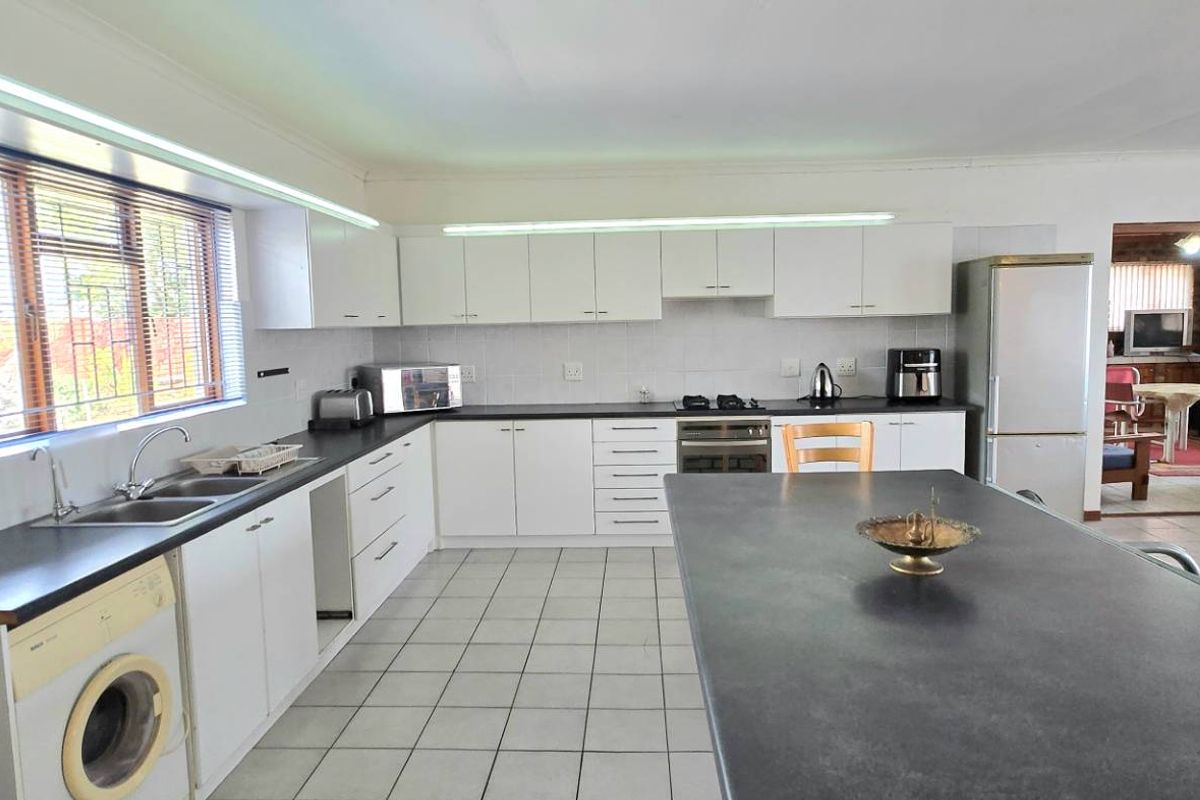 Spacious kitchen featuring white cabinetry, dark countertops, a central island, and integrated laundry appliances, flowing into an adjacent living area.
