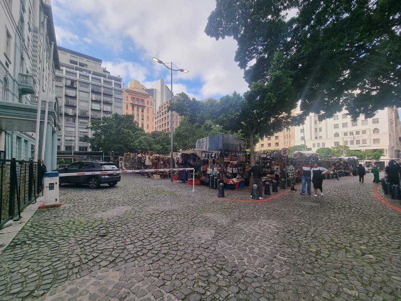 A view of a cobblestone street area featuring a security boom gate, mature trees, and surrounding urban apartment buildings.