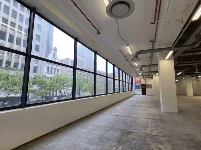 Spacious open-plan retail or office area featuring large windows, exposed industrial ceiling infrastructure, and concrete flooring, offering a versatile blank canvas.