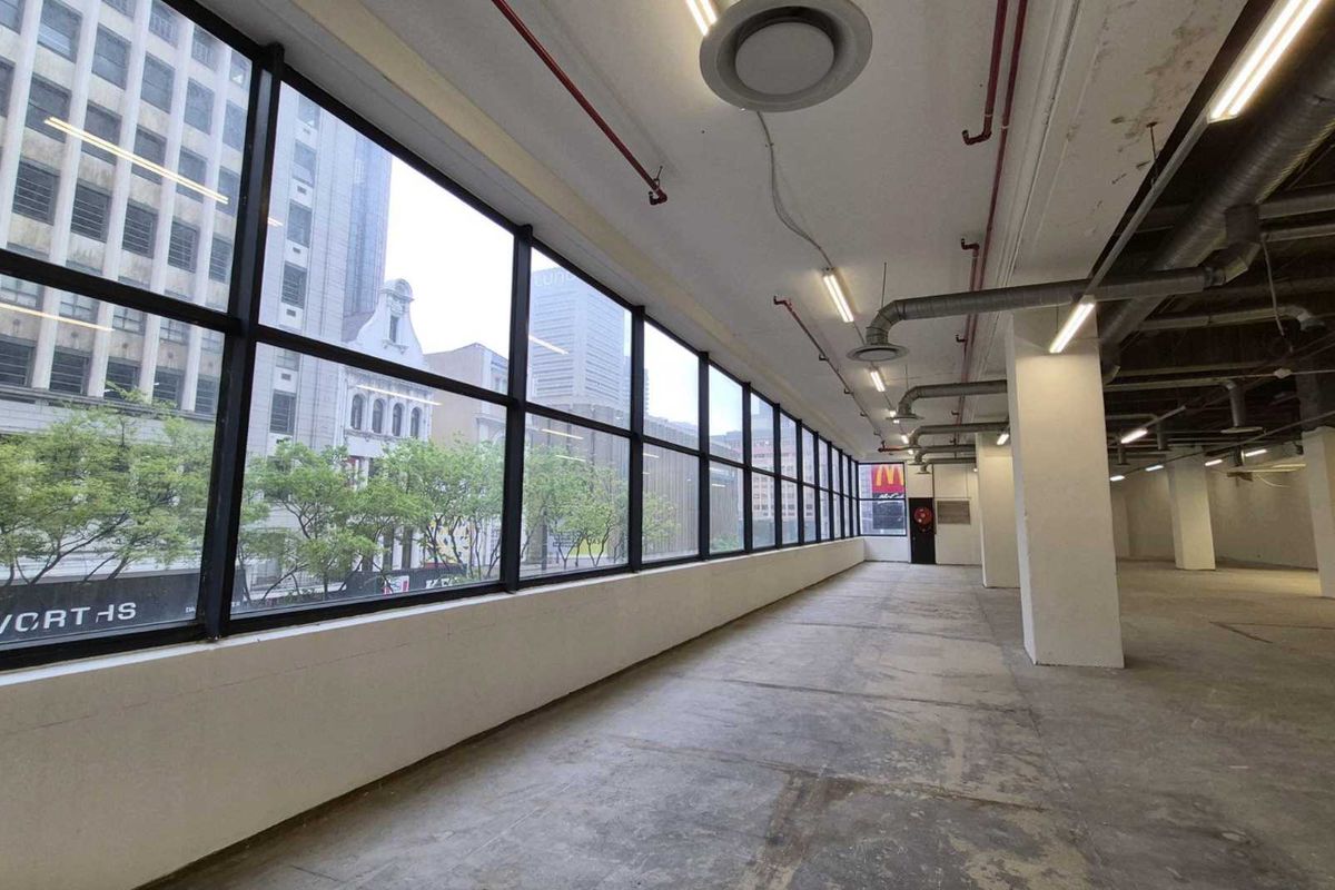 Spacious open-plan retail or office area featuring large windows, exposed industrial ceiling infrastructure, and concrete flooring, offering a versatile blank canvas.