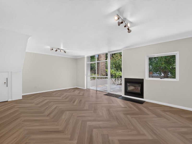 Spacious, light-filled living room featuring modern herringbone flooring, a built-in fireplace, and direct access to the outdoor patio area.