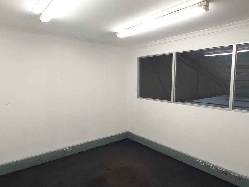 A vacant office space featuring carpet flooring, aluminium framed windows, and functional fluorescent strip lighting, suitable for a professional workspace.