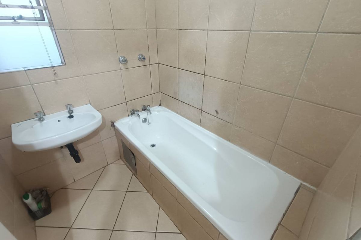 A dated bathroom featuring a standard bathtub, wall-mounted basin, and neutral ceramic tiling throughout, offering a blank canvas for renovation.