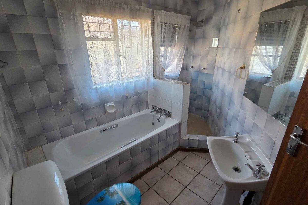 A dated bathroom featuring a bathtub, separate shower enclosure, pedestal basin, and toilet, finished with blue and white wall tiles.
