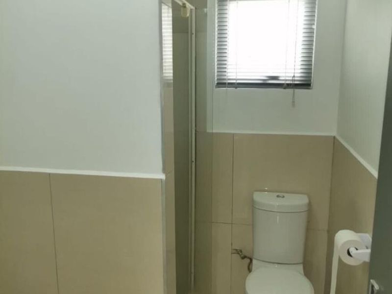 A functional bathroom featuring a shower enclosure, toilet, and neutral wall and floor tiling with a window for natural light.