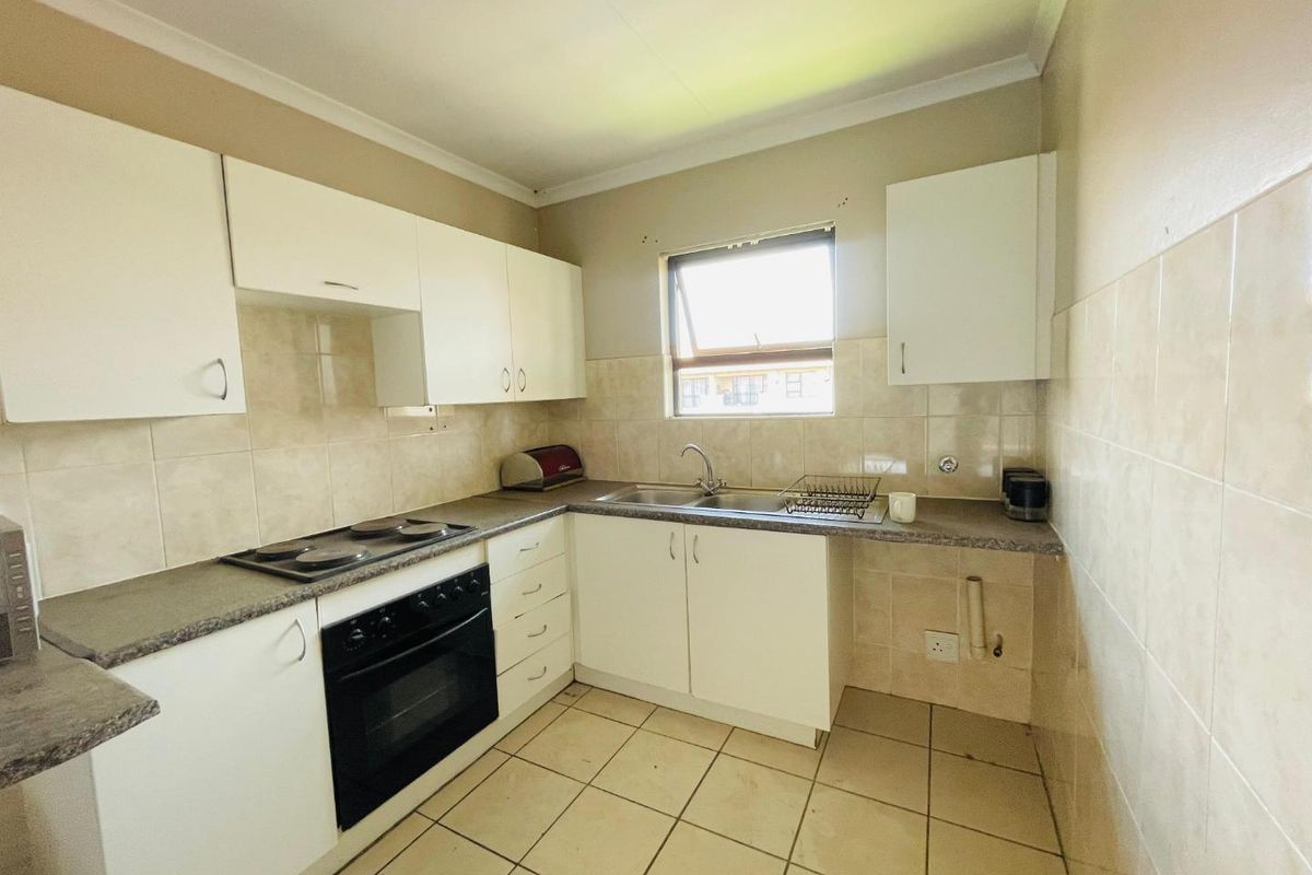 A functional kitchen featuring white cabinetry, a built-in oven and hob, tiled splashbacks, and a stainless steel sink.