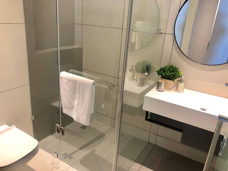 Modern bathroom featuring a glass-enclosed shower, wall-mounted vanity with basin, and contemporary neutral tiling throughout.