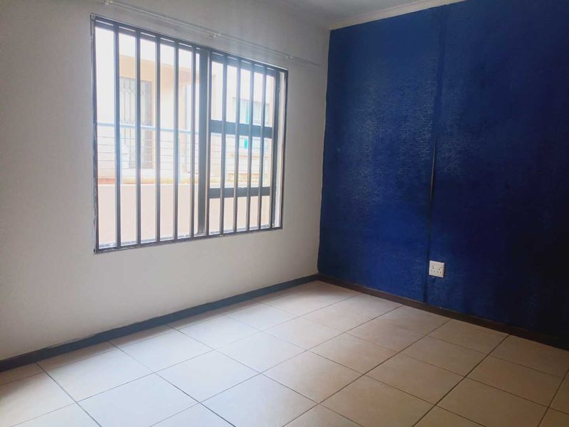 An empty bedroom featuring tiled flooring and a window with security bars, ready for a fresh coat of paint and new interior design.
