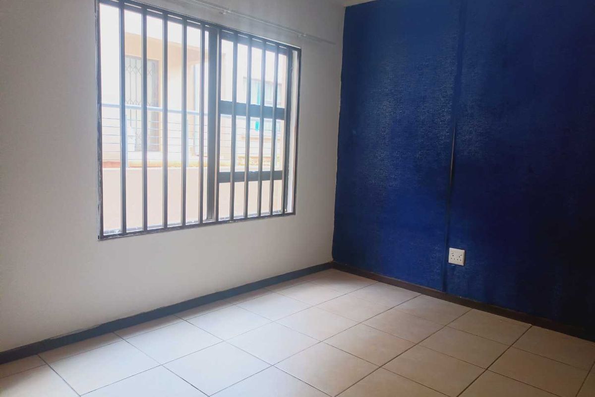 An empty bedroom featuring tiled flooring and a window with security bars, ready for a fresh coat of paint and new interior design.