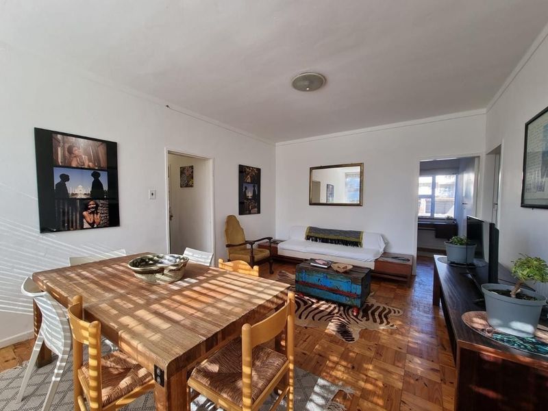 Open plan living and dining area featuring classic parquet flooring and natural light, providing a versatile space for relaxation and entertaining.