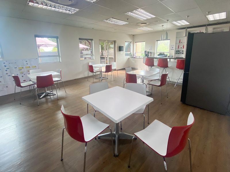 Open-plan industrial breakroom or canteen area featuring laminate flooring, suspended ceilings, and a functional kitchenette counter with built-in shelving.