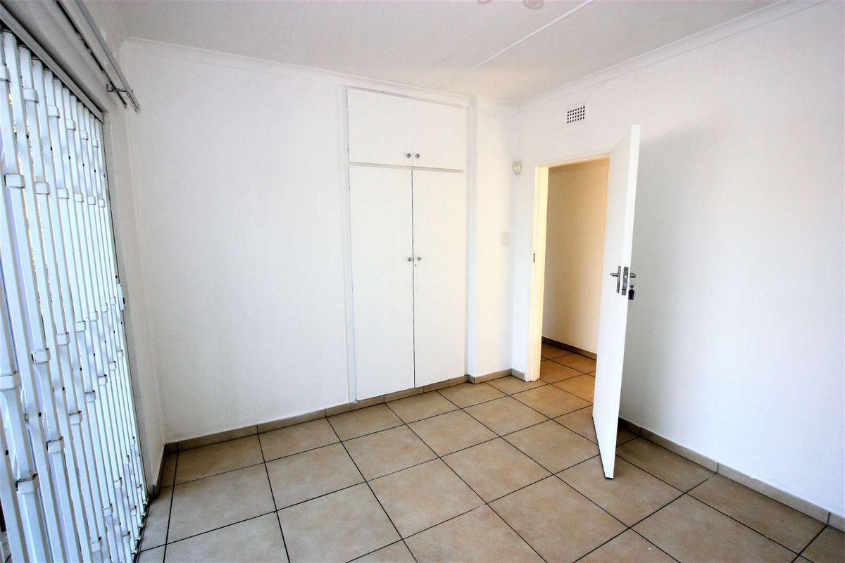 An empty bedroom featuring neutral tiled flooring, built-in cupboards, and a security gate leading to an outdoor area.