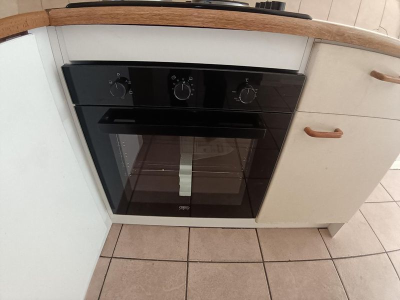 A close-up view of a built-in oven and hob set within a kitchen featuring laminate countertops and tiled flooring.