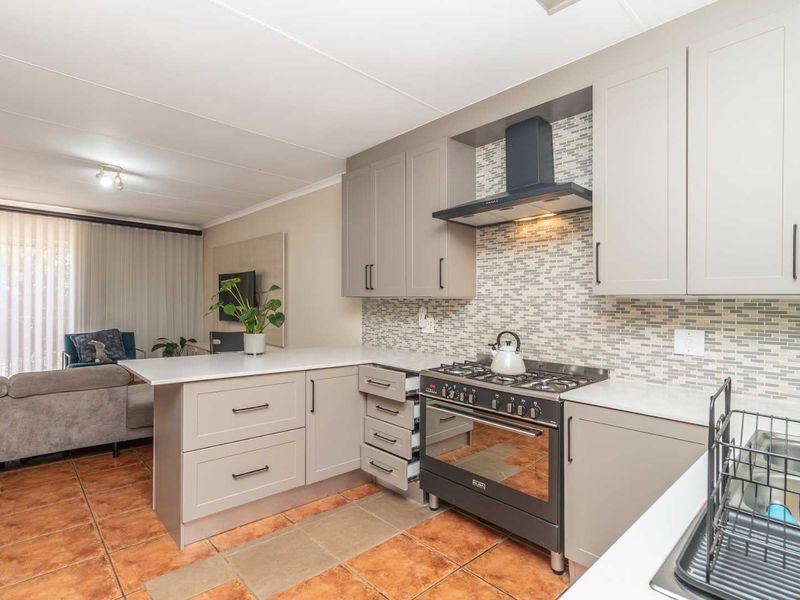 Modern open-plan kitchen featuring neutral cabinetry, a gas stove with extractor fan, mosaic backsplash, and quartz countertops, seamlessly flowing into the living area.