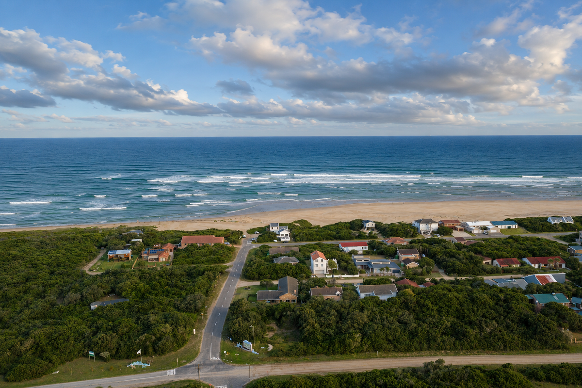 An aerial view of a coastal residential neighborhood situated directly along the beachfront, showcasing the proximity to the ocean and local road infrastructure.