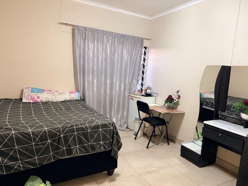 A functional bedroom featuring tiled flooring and a security gate on the window, providing a practical living space.