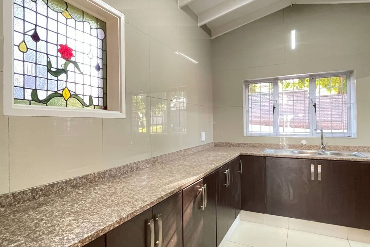 A clean, functional kitchen featuring dark cabinetry, laminate countertops, a stainless steel sink, and a unique stained glass window under a vaulted ceiling.