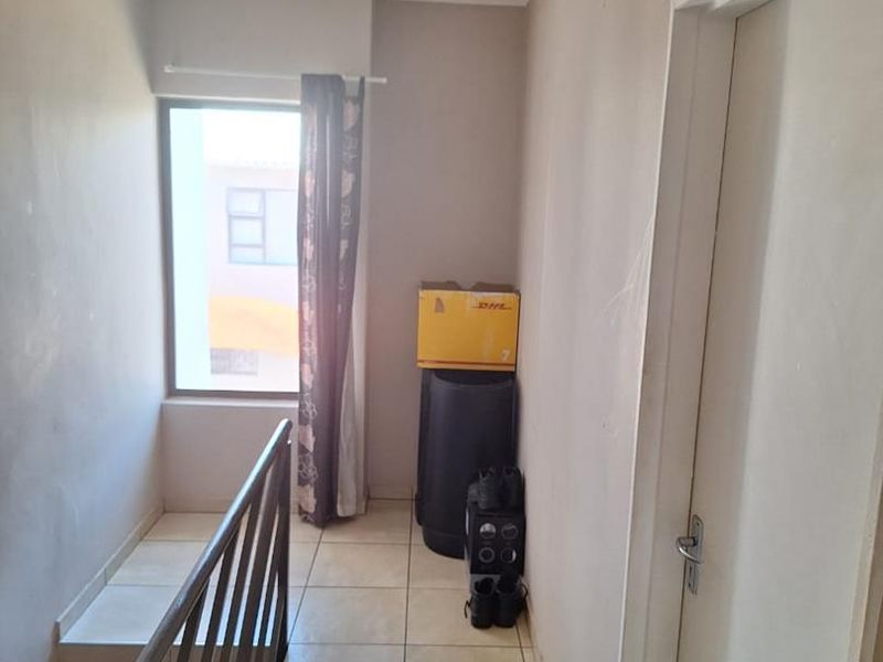 A functional hallway area featuring tiled flooring, a metal staircase railing, and access to an internal door, providing a clean transition between levels.