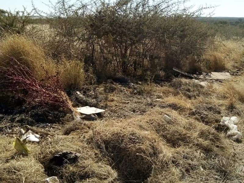 A view of the vacant commercial land featuring dry, overgrown vegetation and scattered debris across the site.