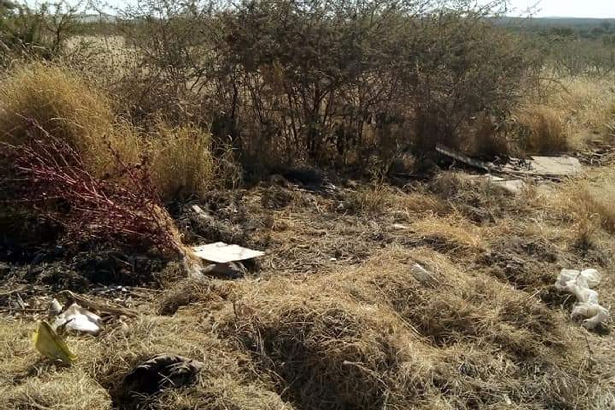 A view of the vacant commercial land featuring dry, overgrown vegetation and scattered debris across the site.
