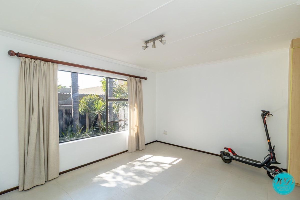 A bright and spacious bedroom featuring neutral tiled flooring, large window with natural light, and a clean, minimalist aesthetic.