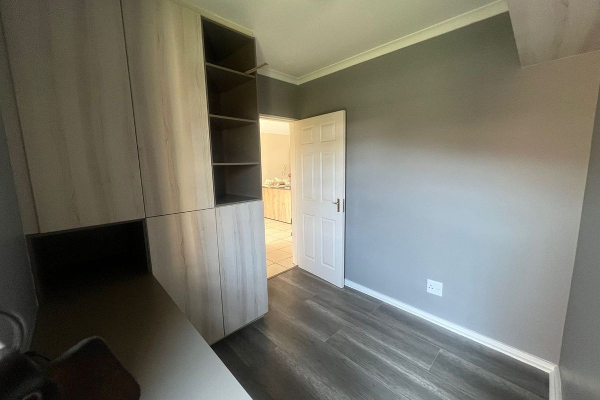 A clean, empty bedroom featuring modern wood-look laminate flooring and built-in storage cabinetry with open shelving.